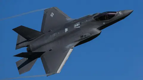 Ảnh: Getty Images. Một chiếc máy bay chiến đấu tàng hình F-35 Lightning II màu đen đang lượn vòng trên bầu trời xanh trong vắt.